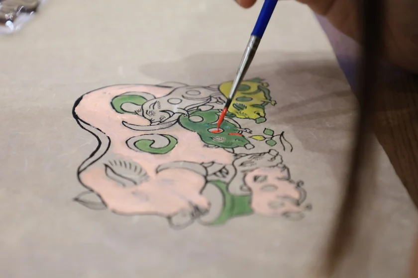 A hand applying a red finish to the surface of Dó paper